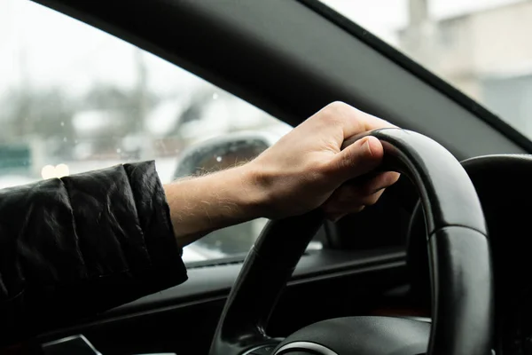 stock image Selective focus mans hand on steering wheel, driving car in winter background. Black luxury modern car Interior. Steering wheel, shift lever and dashboard. Black leather Detail Automatic gear stick