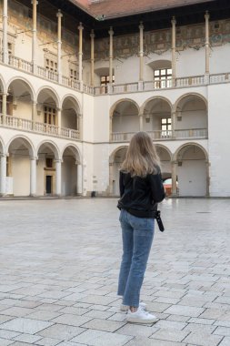 Tarihsel yerlerdeki kadın gezgin Krakow Wawel şatosunun tarihi avlusuna bakıyor. Güneşli bir günde tarihi bir yerde turist. Kadın turizmi ve blog paylaşımı izleyiciler için çevrimiçi