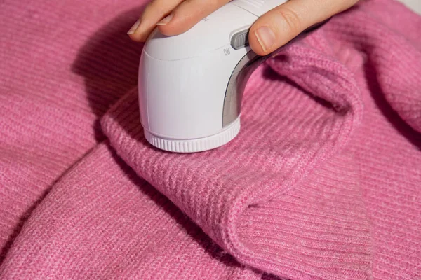 stock image Woman using Anti-pilling razor at home. Device for shaving clothes. Anti-Plush fabric Shaver. Electric portable sweater pill defuzzer Lint remover from pink acrylic or wool sweater. Slow fashion