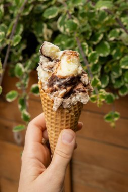 Female hand holding delicious american vanilla chocolate ice cream. Tasty homemade icecream Gelato in the waffle cone. Gluten free vegan dairy free ice cream. 