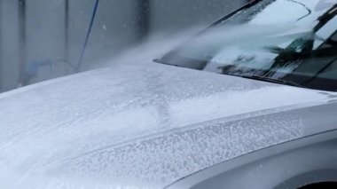 Washing luxury silver car on touchless car wash. Washing sedan car with foam self-service and high pressure water. Winter cleaning in car wash. Cleanliness and order in urban environment