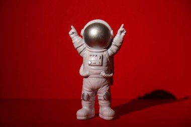 Plastic toy astronaut on colorful red background Copy space. Concept of out of earth travel, private spaceman commercial flights. Space missions and Sustainability