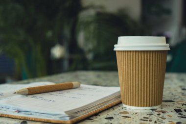 Kağıt not defteriyle kağıt bardakta sıcak latte kahve. Kafe masasında bir paket kağıt bardak. Verimli çalışma ve çalışma için kahveli Freelance Workspace defteri. Rahat çalışıyor.