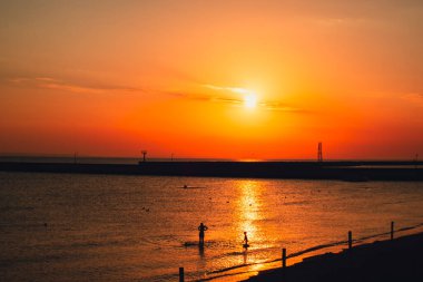 Silhouette of people enjoying sea and summer days. Reflection of sunlight over sea surface at sunset. Orange and gold blue sky. Scenic Gold sea. Dramatic Yellow sun coming out of the sea. Majestic