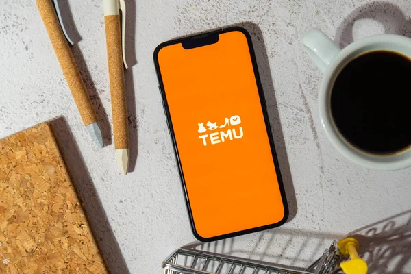 stock image Gdansk, Poland - March 2023 Temu app icon in screen of mobile phone iPhone Apple with shopping cart workplace. Temu subsidiary of China based e-commerce platform Pinduoduo. Online shopping Temu