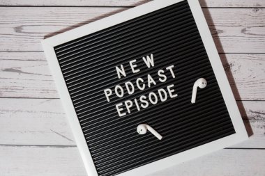 Yeni PODCAST EPISODE yazılı duyuru panosu ahşap masada kablosuz kulaklıklarla. Podcast konsepti. Radyodaki ses iyileştirme sağlık alışkanlıkları.