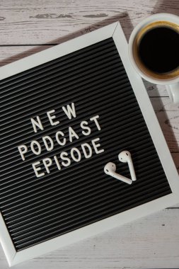 Tahta masada üzerinde yeni PODCAST EPISODE yazılı beyaz kahve fincanı kablosuz kulaklıkla duyuru panosu. Podcast konsepti. Radyodaki ses iyileştirme sağlık alışkanlıkları.