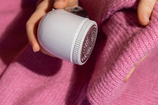 stock image Woman using Anti-pilling razor at home. Device for shaving clothes. Anti-Plush fabric Shaver. Electric portable sweater pill defuzzer Lint remover from pink acrylic or wool sweater. Slow fashion