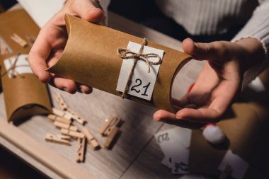 Unrecognizable young woman sticks number on craft bag, fastens with clothespin. Female making kraft paper for homemade advent calendar Made with your own hands step by step DIY crafts do it yourself clipart