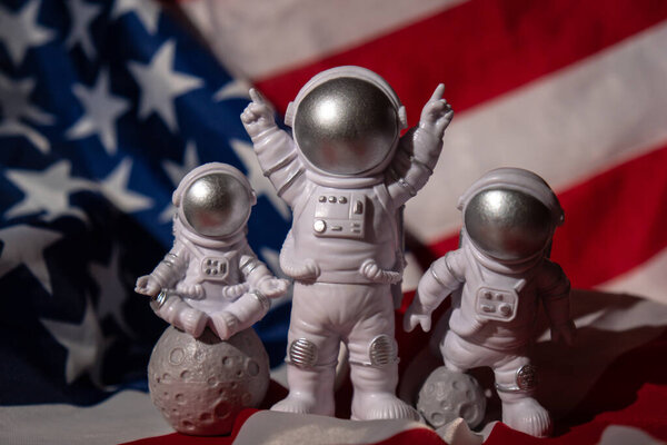 Three Plastic toys figure astronaut on American flag background Copy space. 50th Anniversary of USA Landing on The Moon Concept of out of earth travel, private spaceman commercial flights. Space