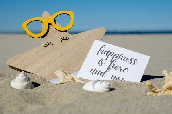 stock image HAPPINESS IS HERE AND NOW text on paper greeting card on background of funny starfish in glasses summer vacation decor. Sandy beach sun coast. Slowing-down, enjoying the moment, good moments, slow