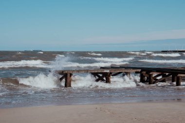 Fırtınalı deniz dalgaları dramatik mavi arka planda boş ahşap iskele. Su sıçratan deniz dalgalarıyla deniz manzarası. Gdansk Polonya 'da kumsal tatili kaçamağı. Metnin için boşluk kopyala 