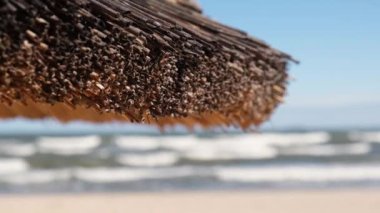 Boş kumsaldaki saman plajı rattan şemsiyesini kapatın. Mavi gökyüzü arka planda, deniz kıyısında. Rahatlatıcı bir gün. Idyllic seyahat ve yaz tatili konsepti. Güzel tropikal bölgelerde saman şemsiyesi