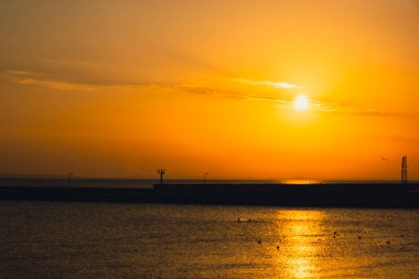 Güneş ışığının günbatımında deniz yüzeyine yansıması. Turuncu ve altın rengi mavi gökyüzü. Manzaralı altın deniz. Denizden dramatik sarı güneş geliyor. Muhteşem yaz manzarası