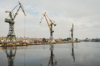 Motlawa river to Baltic Sea. Coal mine, polluting environment by the river POV from ferry swimming on river canal. Industrial building at the Gdansk Shipyard. Prefabrication workshop and heavy cranes