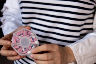 Woman sorting pills Organizer weekly shots Closeup of medical pill box with doses of tablets for daily take medicine with white pink drugs and capsules. Young woman getting her daily vitamins at home