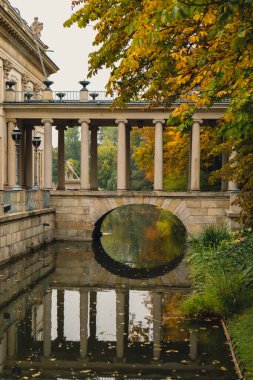 Baths classicist Palace on the Isle in Lazienki Park touristic place in Warsaw. Lazienki Royal Baths Park, Warsaw Poland. Colorful Autumn Foliage and Mirror Reflection on the Lake. Yellow leaves