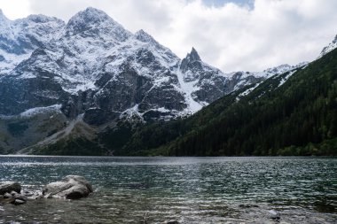Polonya Tatry dağlarındaki Morskie Oko Gölü Karlı Dağ Kulübesi, Zakopane, Polonya. Güzel yeşil tepeler ve kara bulutlar içindeki dağlar ve Morskie Oko Gölü 'nün yansıması. Seyahat eden turist