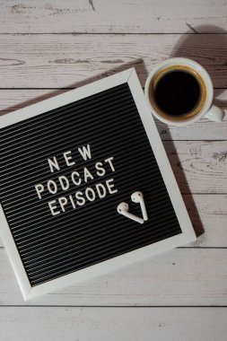 Tahta masada üzerinde yeni PODCAST EPISODE yazılı beyaz kahve fincanı kablosuz kulaklıkla duyuru panosu. Podcast konsepti. Radyodaki ses iyileştirme sağlık alışkanlıkları.