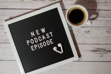 Tahta masada üzerinde yeni PODCAST EPISODE yazılı beyaz kahve fincanı kablosuz kulaklıkla duyuru panosu. Podcast konsepti. Radyodaki ses iyileştirme sağlık alışkanlıkları.