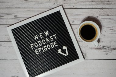 Tahta masada üzerinde yeni PODCAST EPISODE yazılı beyaz kahve fincanı kablosuz kulaklıkla duyuru panosu. Podcast konsepti. Radyodaki ses iyileştirme sağlık alışkanlıkları.