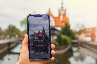 Tarihi yerler avlusunda gezgin bir kadın ve telefonda kısa video çekiyor. Gdansk Polonya 'da güneşli bir günde tarihi yerleri gösteren turist fotoğrafları. Tanınmayan kadın turizmi ve blog yazarlığı