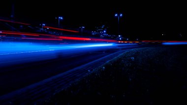 Geceleri arabaların ışıkları. Sokak lambaları. Gece Karayolu Şehri. Uzun pozlu fotoğraf gece yolu. Yoldaki renkli kırmızı ışık şeritleri. Arkaplan duvar kağıdı odaklı olmayan fotoğraf. 