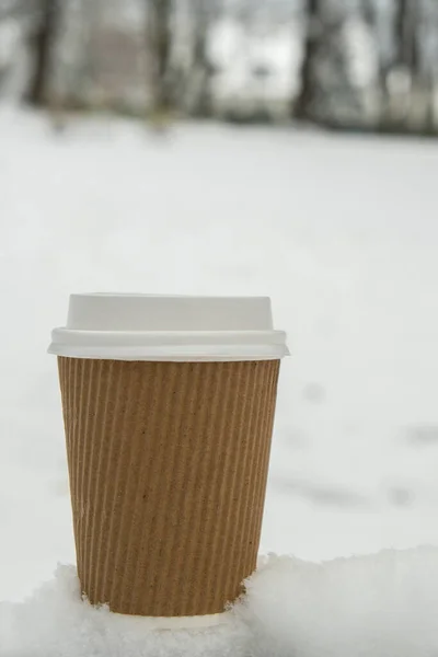 Hot warming drink in Eco paper cup. Mock up Cardboard coffee or tea Cup in the snow in winter day. Copy space Creative trendy zero waste recycle cup white snow-covered field