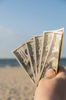 Kumlu sahil şeridinde nakit para gösteren tanınmayan bir kadın. Tatil için para biriktirme kavramı. Seyahat tatillerinde maliyetli. Ekstra para, pasif gelir