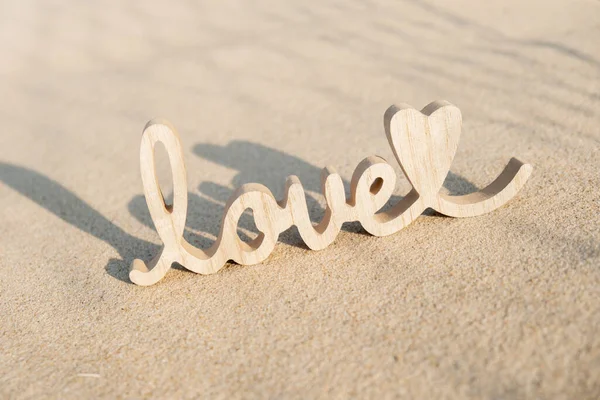 Wooden word love on sandy beach background. Concept of romantic holiday anniversary, proposal, valentines day greeting card, postcard. Letter text in tropical vacation Sand surface. Deep shadows Love