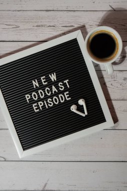Tahta masada üzerinde yeni PODCAST EPISODE yazılı beyaz kahve fincanı kablosuz kulaklıkla duyuru panosu. Podcast konsepti. Radyodaki ses iyileştirme sağlık alışkanlıkları.