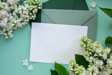 Boş yeşil zarflı kompozisyon ve nane arkaplanda güzel bahar leylak çiçekleri. Mockup kart davetiyesi tebrik kartı posta kartı kopyalama alanı şablonu boş. Çiçek açan leylak dalları