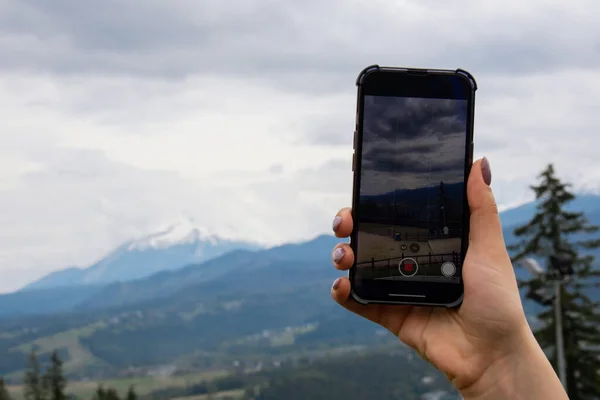 Mobile phone shooting video for social media. Tourist blogger travel hand making memories Snowy mountains, green forests In National park. Mountain nature landscape. Travel outdoors green tourism