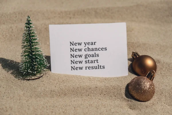 NEW YEAR CHANCES GOALS START RESULTS text on paper greeting card on background sandy beach sun coast. Christmas balls Santa hat New Year New Me Resolutions decoration. Summer vacation decor. Holiday