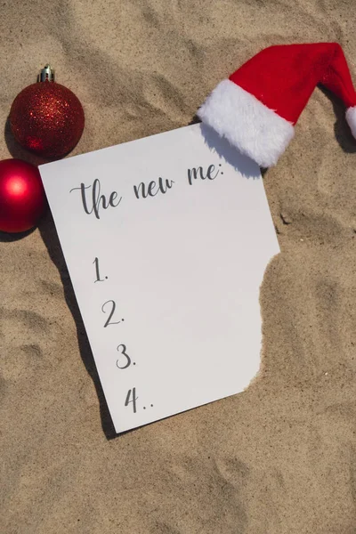 THE NEW ME text on paper greeting card on background sandy beach sun coast. Christmas balls Santa hat New Year New Me Resolutions decoration. Summer vacation decor. Holiday concept calendar date