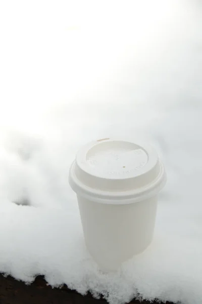 Hot warming drink in Eco paper cup. Mock up Cardboard coffee or tea Cup in the snow in winter day. Copy space Creative trendy zero waste recycle cup white snow-covered field