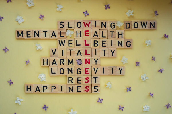 Верхний вид слова WELLNESS на желтом фоне с цветами. Минимализм творческий кроссворд концепции. Послание к тексту Замедление психического здоровья жизнеспособность жизнеспособность гармония долговечность отдыха