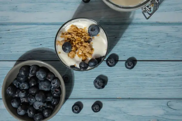 Morning granola breakfast with homemade greek yogurt, blueberries in glasses on blue wooden background. Healthy diet Crunchy granola with yogurt nuts and blueberries for healthy light breakfast