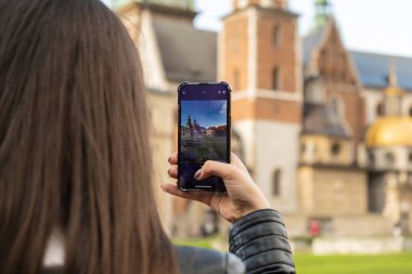 Female traveler in historical places looks around courtyard of landmark and shoots short video on phone. Tourist photographs historic place on sunny day. Unrecognizable woman Tourism and blogging