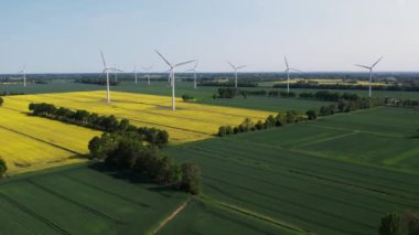 Hava manzaralı rüzgar santrali elektrik üretiyor. Yenilenebilir yeşil temiz enerji. Kırsal bölgedeki bulutlu mavi gökyüzüne karşı çimenli sarı kanola tarlasında sürdürülebilir canlı rüzgâr türbini. Açıklar