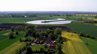 Kırsal bölge Gdansk Polonya Avrupa 'sında, bulutlu mavi gökyüzüne karşı çimenli sarı çiftlik kanola tarlası üzerinde hava manzarası. Evler ve nehir sürdürülebilir yaşam