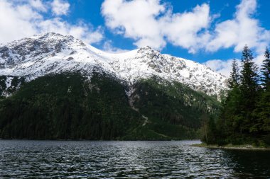 Polonya Tatry dağlarındaki Morskie Oko Gölü Karlı Dağ Kulübesi, Zakopane, Polonya. Güzel yeşil tepeler ve kara bulutlar içindeki dağlar ve Morskie Oko Gölü 'nün yansıması. Seyahat eden turist