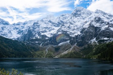 Morskie Oko lake Snowy Mountain Hut in Polish Tatry mountains, Zakopane, Poland. Beautiful green hills and mountains in dark clouds and reflection on the lake Morskie Oko lake. Travel tourist