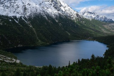 Polonya Tatry dağlarındaki Morskie Oko Karlı Dağ Kulübesi, insansız hava aracı manzarası, Zakopane, Polonya. Güzel yeşil tepelerin ve dağların kara bulutlardaki görüntüsü ve Morskie Oko Gölü 'nün yansıması.