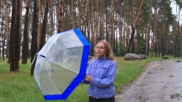 森の外に透明な青い傘を持っている若い女性 傘を使用して雨の日を遅く動かします いつ雨が降るかチェックする手を持つ女性 予測する — ストック動画