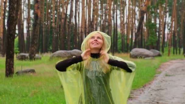 秋の森を歩く黄色いレインコートの笑顔の女性は 雨天を屋外で楽しんでいます 女性観光客が雨季に公園を発見 自然に近づいている メンタルヒーリングフルフィルメントクリーンエアー — ストック動画