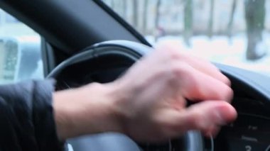 Selective focus mans hand on steering wheel, driving car in winter background. Black luxury modern car Interior. Steering wheel, shift lever and dashboard. Black leather Detail Automatic gear stick