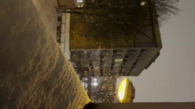 Geceleri yavaş yavaş kar yağıyor. Hava tahmini. Geceleri yerleşim bölgesine kar yağıyor. Kar fırtınasında şehir avlusu manzarası. Sokak lambaları ve karla kaplı bir gece kasabası sokağı. Kar yağışıweather condition