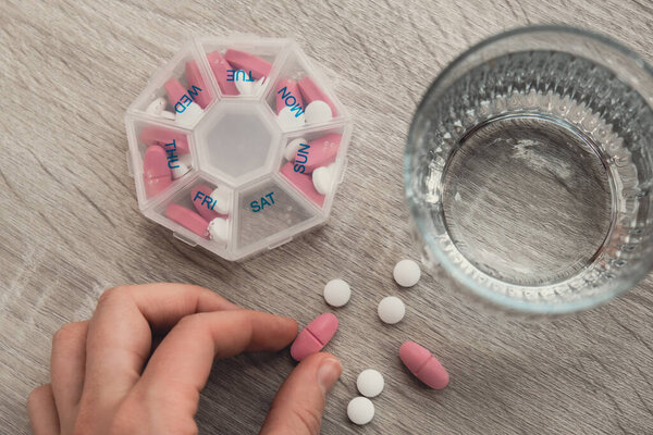 Woman sorting pills Organizer weekly shots Closeup of medical pill box with doses of tablets for daily take medicine with white pink drugs and capsules. Young woman getting her daily vitamins at home