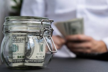 Dolar banknotu cam kavanozda para biriktiriyor. Tanınmayan adam, Orta Yol Tüketim ve Ekonomi Biriktirme İşletme Finansmanı kavramında para hesapladı